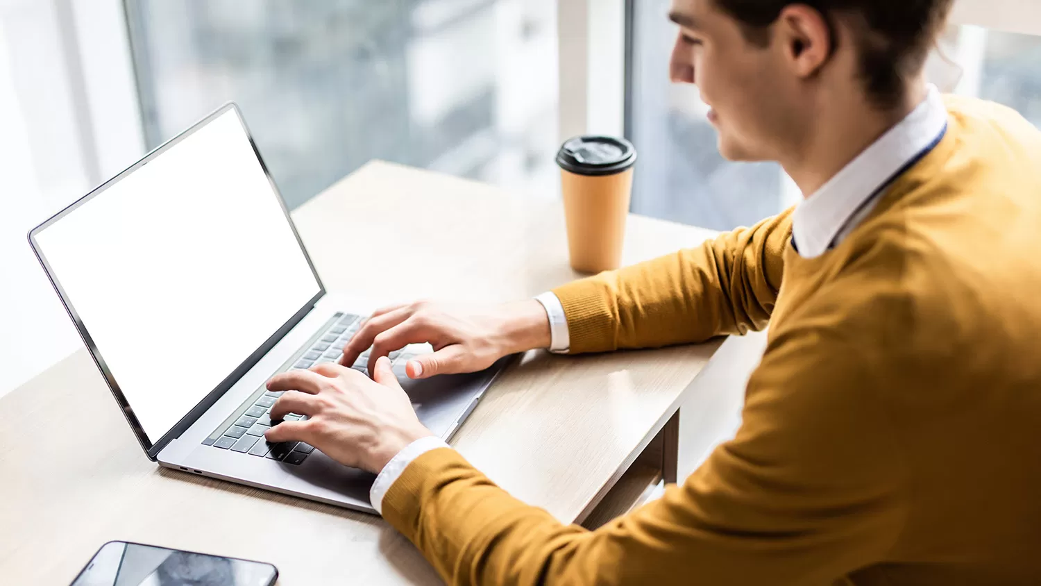 Male sitting down at a desk typing on laptop